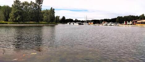 Un lago tranquilo con barcos amarrados en la orilla, rodeado de árboles y un edificio con techo inclinado.