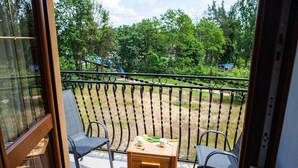 Un balcón con dos sillas, una mesita y vista a un parque con árboles y un parque infantil.