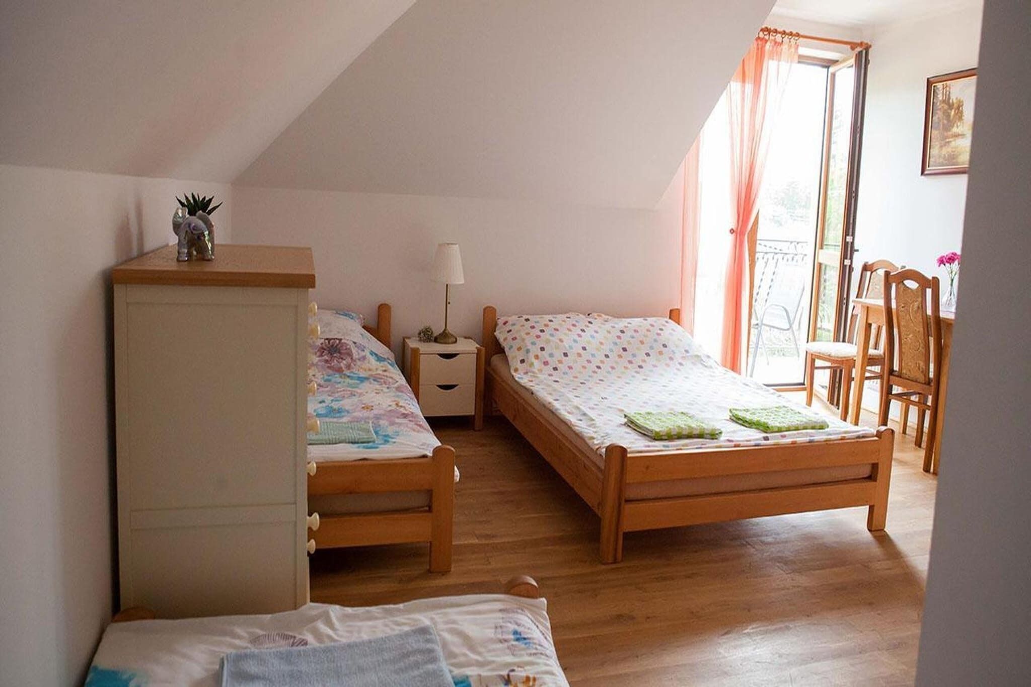Ein Schlafzimmer mit zwei Holzbett, einem Nachttisch, einer Kommode, einem Fenster mit Vorhängen und einem Sessel.