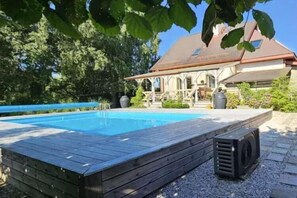 Una piscina con cubierta de madera, un patio techado y un edificio con techo inclinado al fondo.