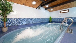 Une piscine intérieure dotée d’un plafond en bois, de murs carrelés et d’une échelle de piscine en métal.