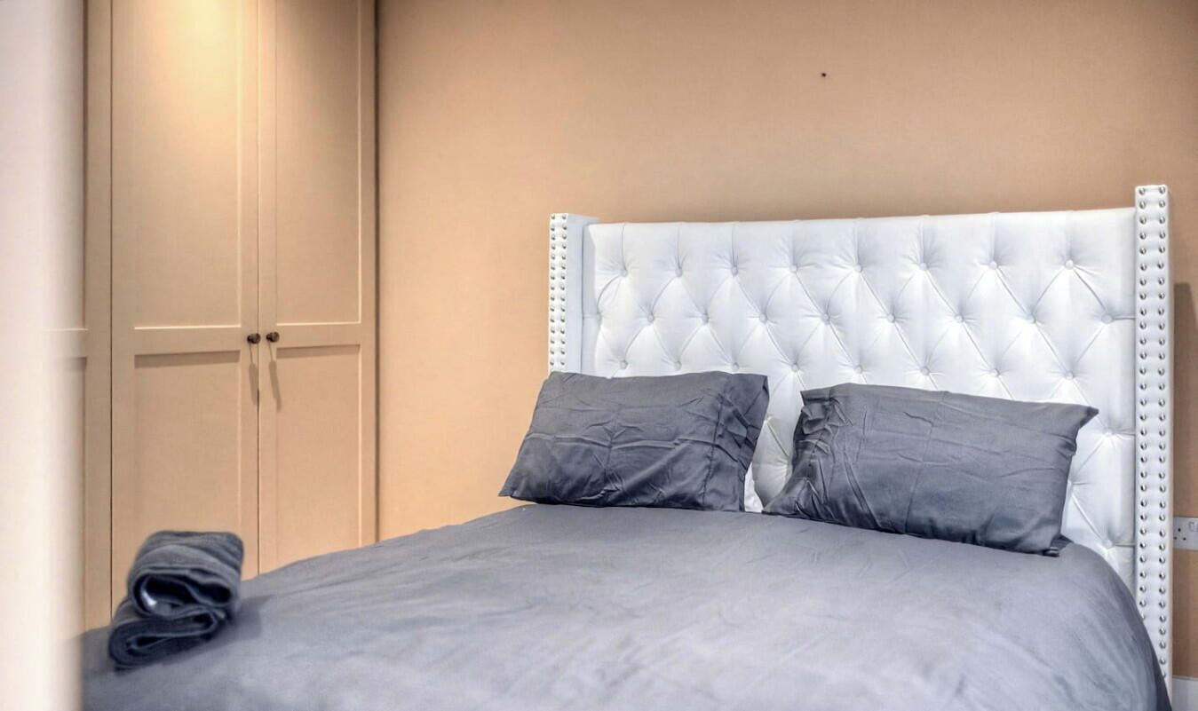 Un lit avec une tête de lit capitonnée, deux oreillers et une couverture pliée.