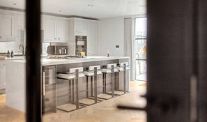 A modern kitchen with white cabinetry, a central island with bar stools, and a large window providing natural light. - Whim Brook Stay - Free parking! (Cheshire East)