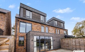 A modern two-story house with a brick facade, large windows, and a wooden deck. - Whim Brook Stay - Free parking! (Cheshire East)