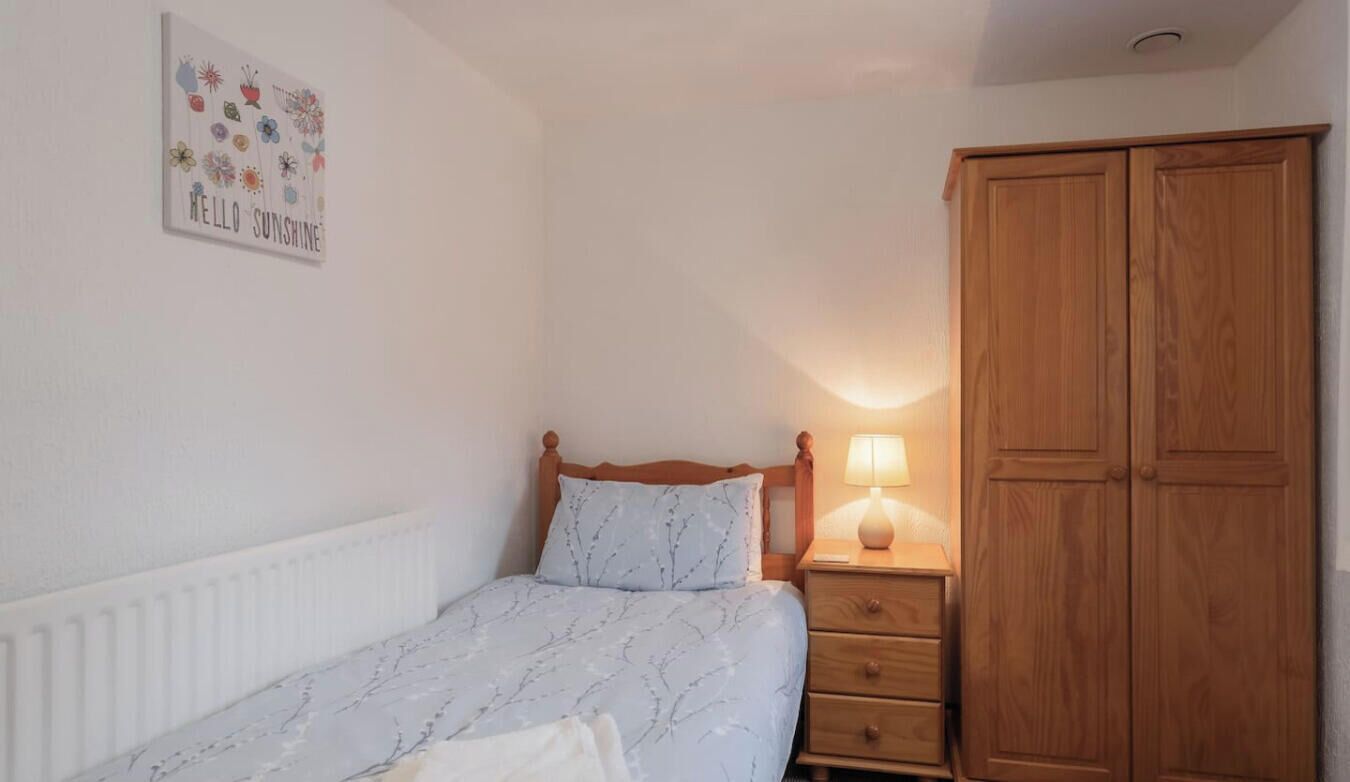 A bedroom with a bed, bedside table with a lamp, a wardrobe, and a wall decoration.
