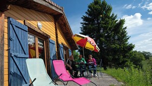 A wooden building with blue shutters, outdoor seating with a red and yellow umbrella, and a gravel path. - A serene interlude in the heart of the Jura mountains (Lent)