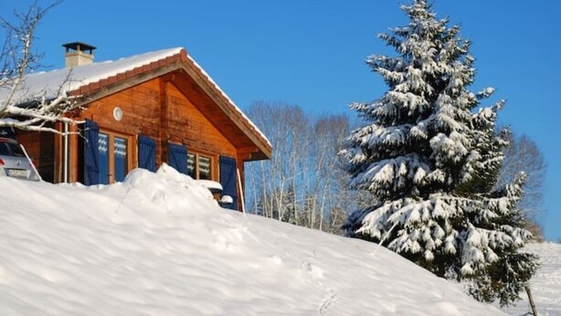 A wooden cabin with a sloped roof, surrounded by snow-covered ground and a snow-laden evergreen tree. - A serene interlude in the heart of the Jura mountains (Lent)