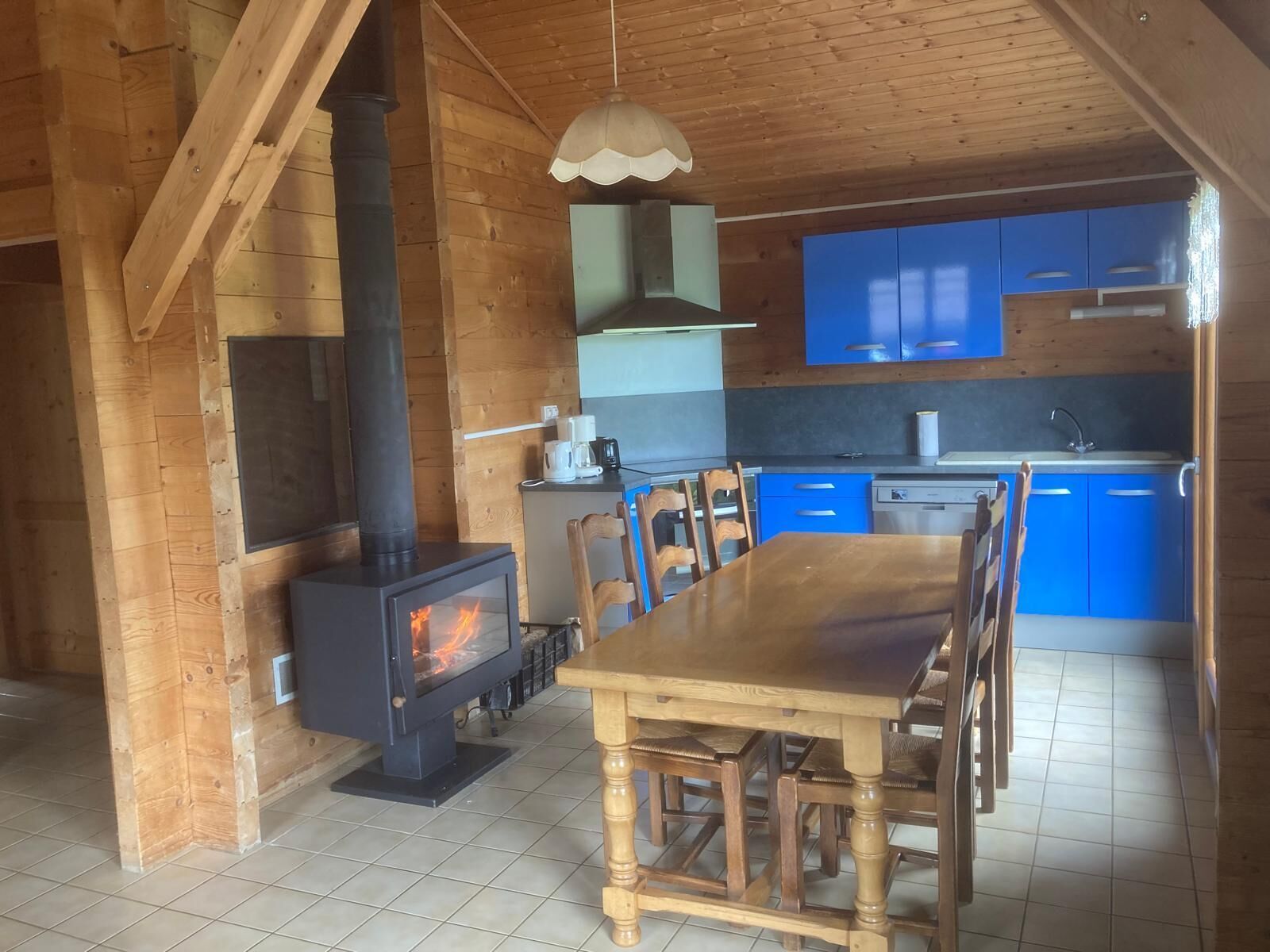 Een houten interieur met een centrale tafel, stoelen, een fornuis en blauwe kasten.