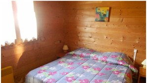 A wooden cabin room with a bed, a small table, and a painting on the wall. - A serene interlude in the heart of the Jura mountains (Lent)