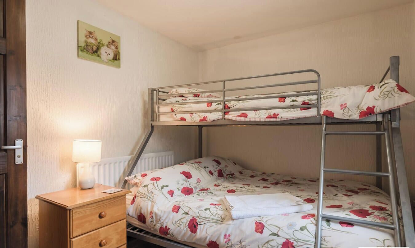 Ein Etagenbett mit Blumenbettwäsche, ein Nachttisch mit Lampe und eine kleine Kommode.