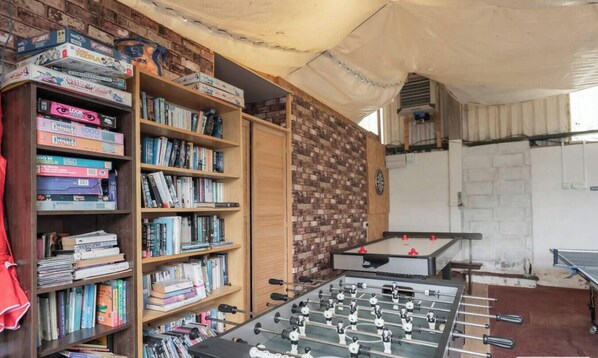 Una habitación con pared de ladrillo, mesa de fútbol de mesa y estanterías llenas de libros.