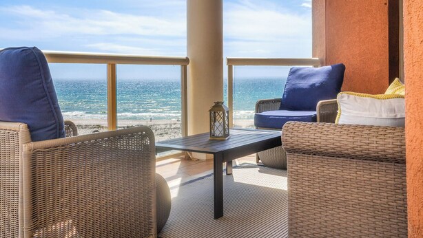 Ein Balkon mit Korbmöbeln, einem kleinen Tisch und Blick aufs Meer.