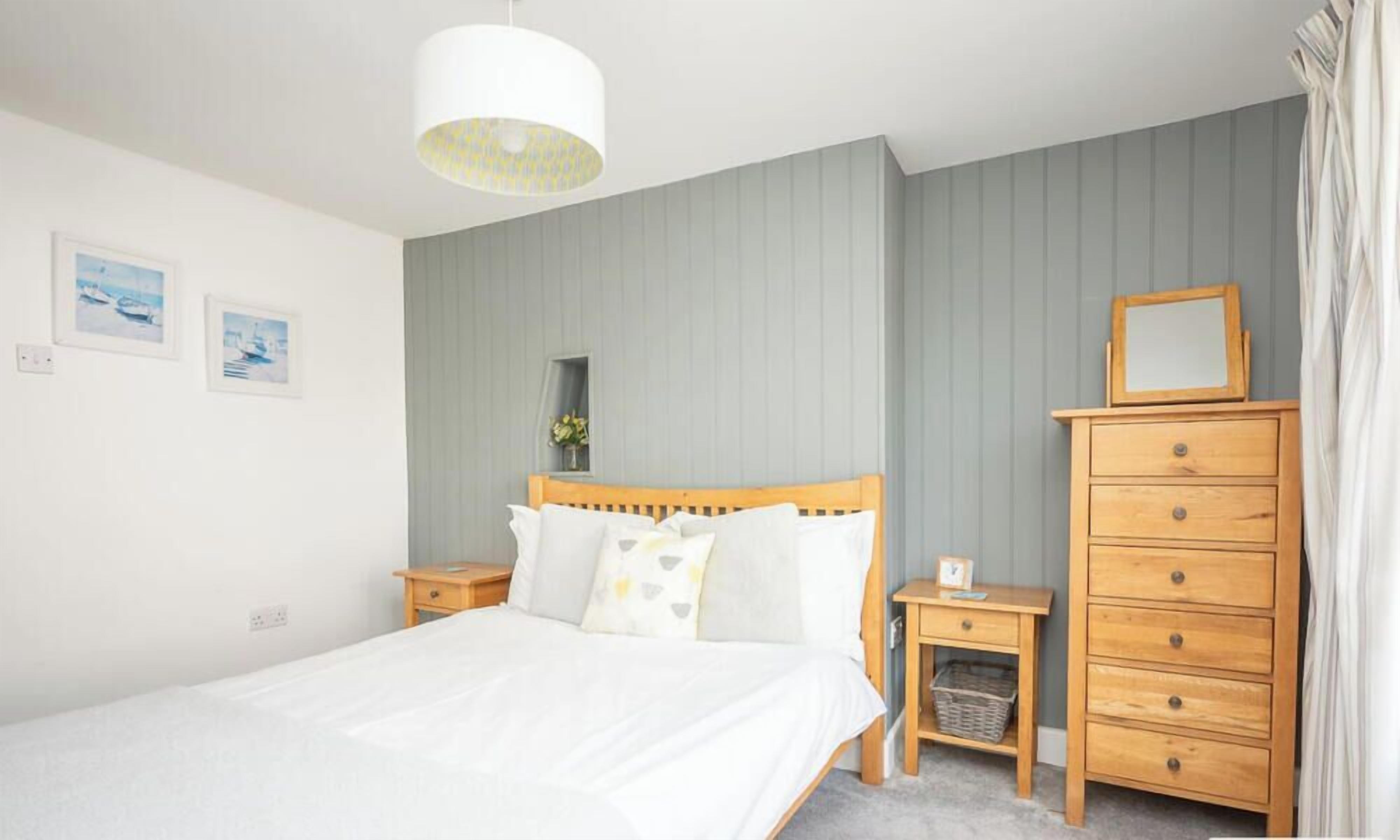 A bedroom with a bed, wooden dresser, nightstands, a hanging light fixture, and two framed pictures on the wall.