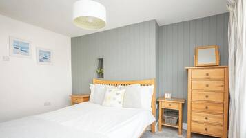 A bedroom with a bed, wooden dresser, nightstands, a hanging light fixture, and two framed pictures on the wall.