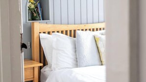 Un dormitorio con cama, mesita de noche, estante con libros y flores, y pared con líneas verticales.