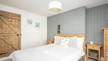 Een slaapkamer met een houten bed, nachtkastje, wandspiegel en een houten kledingkast.