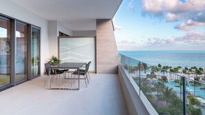 En moderne balkon med spisebord og stole, der giver udsigt over pool og strand.