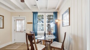 Ein Essbereich mit einem runden Glastisch, Holzstühlen, einem gemusterten Teppich, einer Tür mit Vorhang und einem Fenster mit blauen Vorhängen.