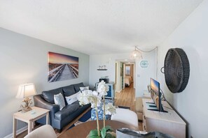 Ein Wohnzimmer mit einer Couch, einem kleinen Tisch, einer Lampe, einer Zimmerpflanze und einem Bild an der Wand.