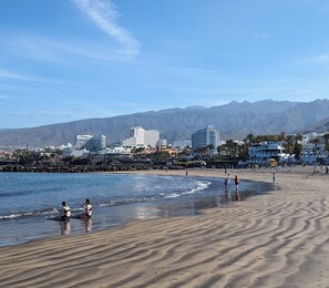 Uma praia com pessoas, um hotel e montanhas ao fundo.