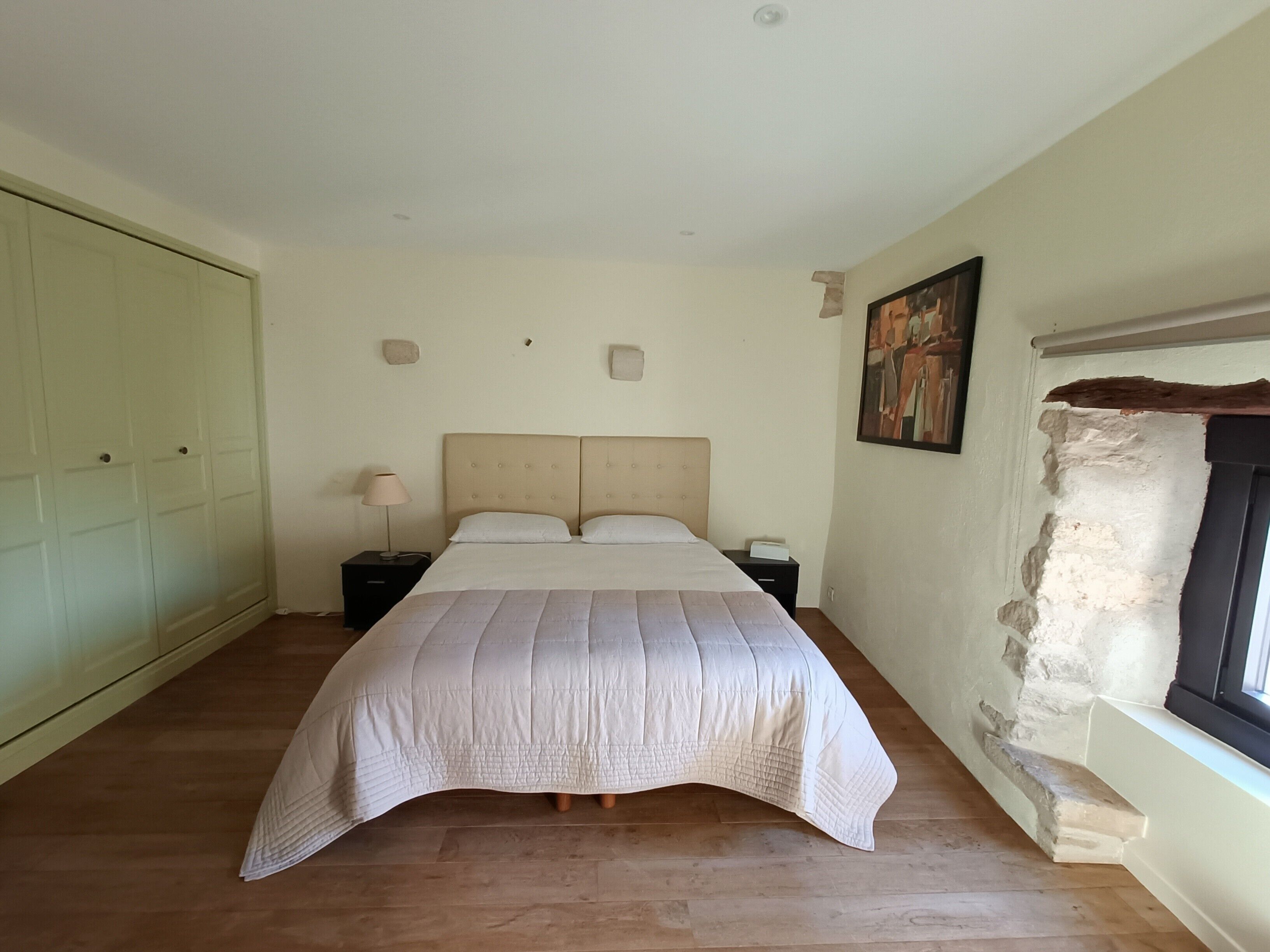Un dormitorio con cama, mesitas de noche, armario, pared de piedra y un cuadro.