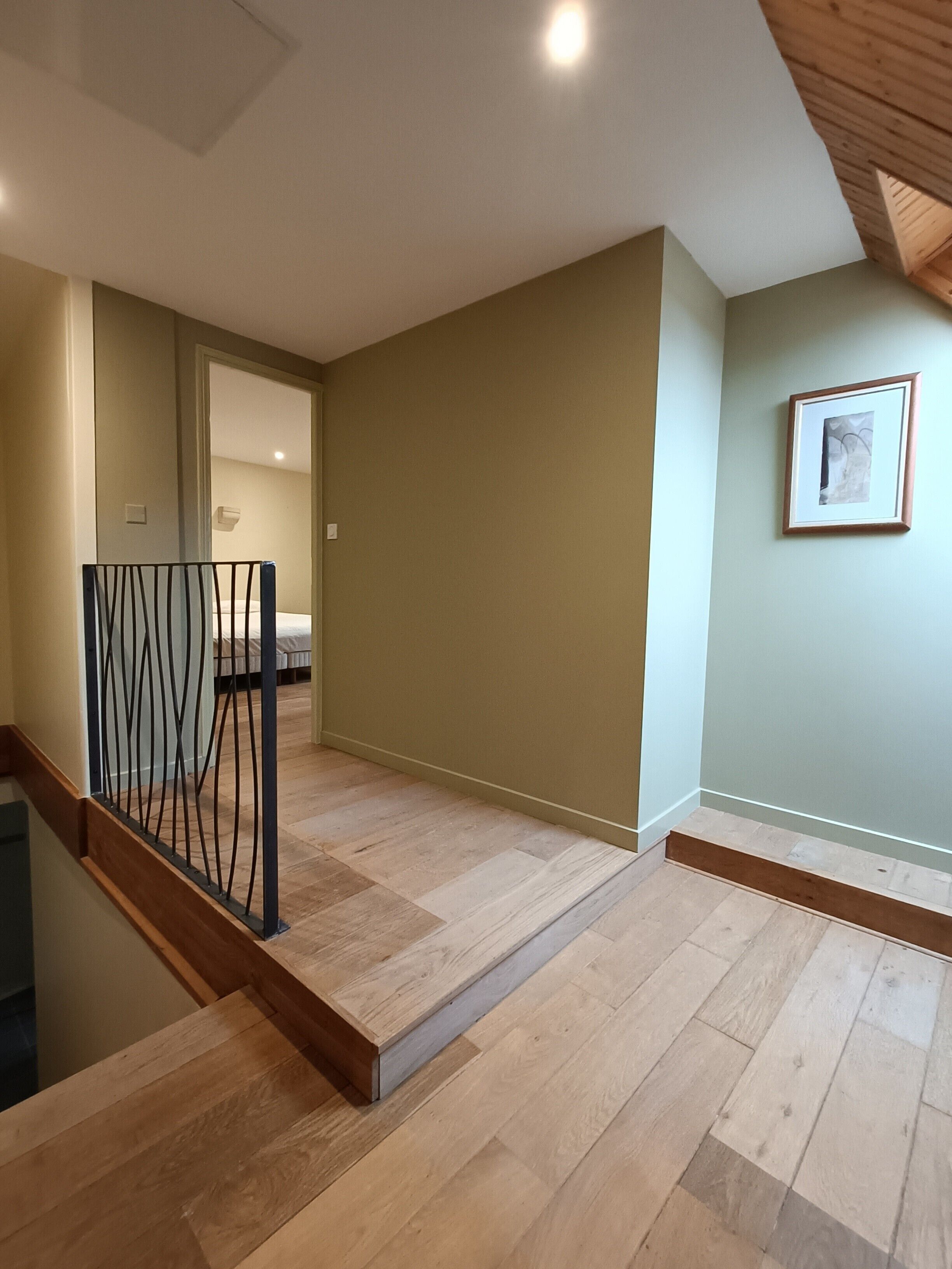 Un escalier avec une rampe en bois mène à une pièce où se trouve un lit et un tableau encadré au mur.
