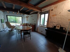 Une pièce comprenant une table à manger en bois, des chaises, un canapé, un piano et une fenêtre avec des rideaux.