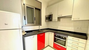 Cucina con pensili bianchi, frigorifero in acciaio inox, microonde e piano cottura.