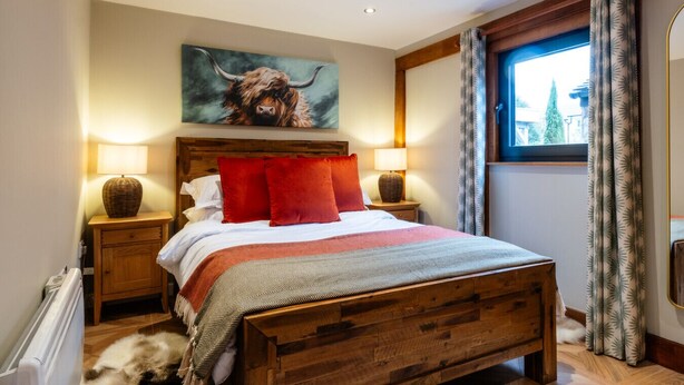 Een slaapkamer met een houten bed, rode kussens, een groot schilderij van een stier en een raam met gordijnen.