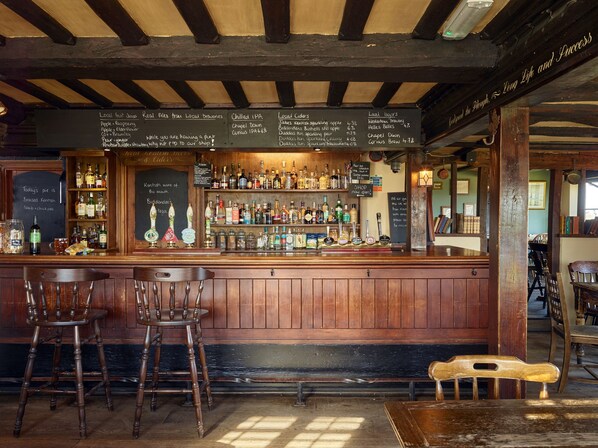 A bar area with wooden furniture, a variety of bottles, and a chalkboard menu. - The Plough Inn (Faversham)