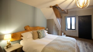 Ein Schlafzimmer mit hölzernem Kopfteil, einem Bett mit weißer Bettwäsche, einem Nachttisch mit Lampe und einer Treppe, die zu einer weiteren Ebene führt.