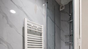 A modern bathroom with a glass-enclosed shower, marble walls, and a wooden floor. - Charmant Studio Paris 15eme - Proche Tour Eiffel (Paris)