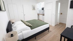 A bedroom with a bed, bedside table, lamp, and a view into the kitchen. - Charmant Studio Paris 15eme - Proche Tour Eiffel (Paris)