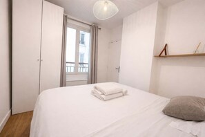 A hotel room with a bed, a window with curtains, a door, and a wall-mounted shelf. - Appartement cosy Paris 11 - Métro à pied - 2p (Paris)