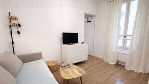 A living room with a sofa, a coffee table, a TV on a white dresser, and a wicker basket. - Appartement cosy Paris 11 - Métro à pied - 2p (Paris)