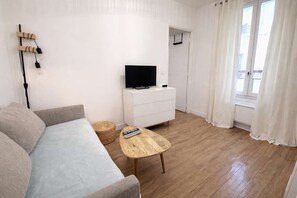 A living room with a sofa, a coffee table, a TV on a white dresser, and a wicker basket. - Appartement cosy Paris 11 - Métro à pied - 2p (Paris)