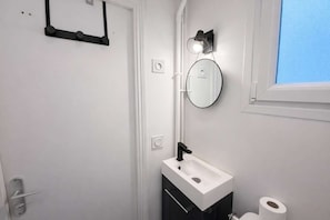 Een badkamer met een witte wastafel, een ronde spiegel, een handdoekhouder en een raam.