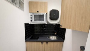A compact kitchen with a built-in oven, a microwave, a sink, and black tiled backsplash. - Appartement cosy Paris 11 - Métro à pied - 2p (Paris)