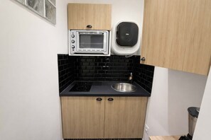 A compact kitchen with a built-in oven, a microwave, a sink, and black tiled backsplash. - Appartement cosy Paris 11 - Métro à pied - 2p (Paris)