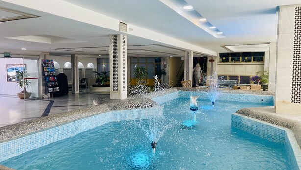 An indoor pool with multiple fountains, a reception area with a 'SALIDA' sign, and a staircase leading to an upper level. - Estudio Minerva Splash by At Home Costa del Sol (Benalmádena)