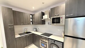 Eine moderne Küche mit dunklen Holzschränken, einem Edelstahlkühlschrank, einer eingebauten Mikrowelle, einem Geschirrspüler und einer Waschmaschine.