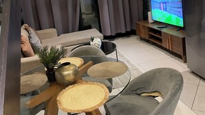 Ein modernes Wohnzimmer mit einer Couch, Sesseln, einem Couchtisch, einem Fernseher und einem Kühlschrank.