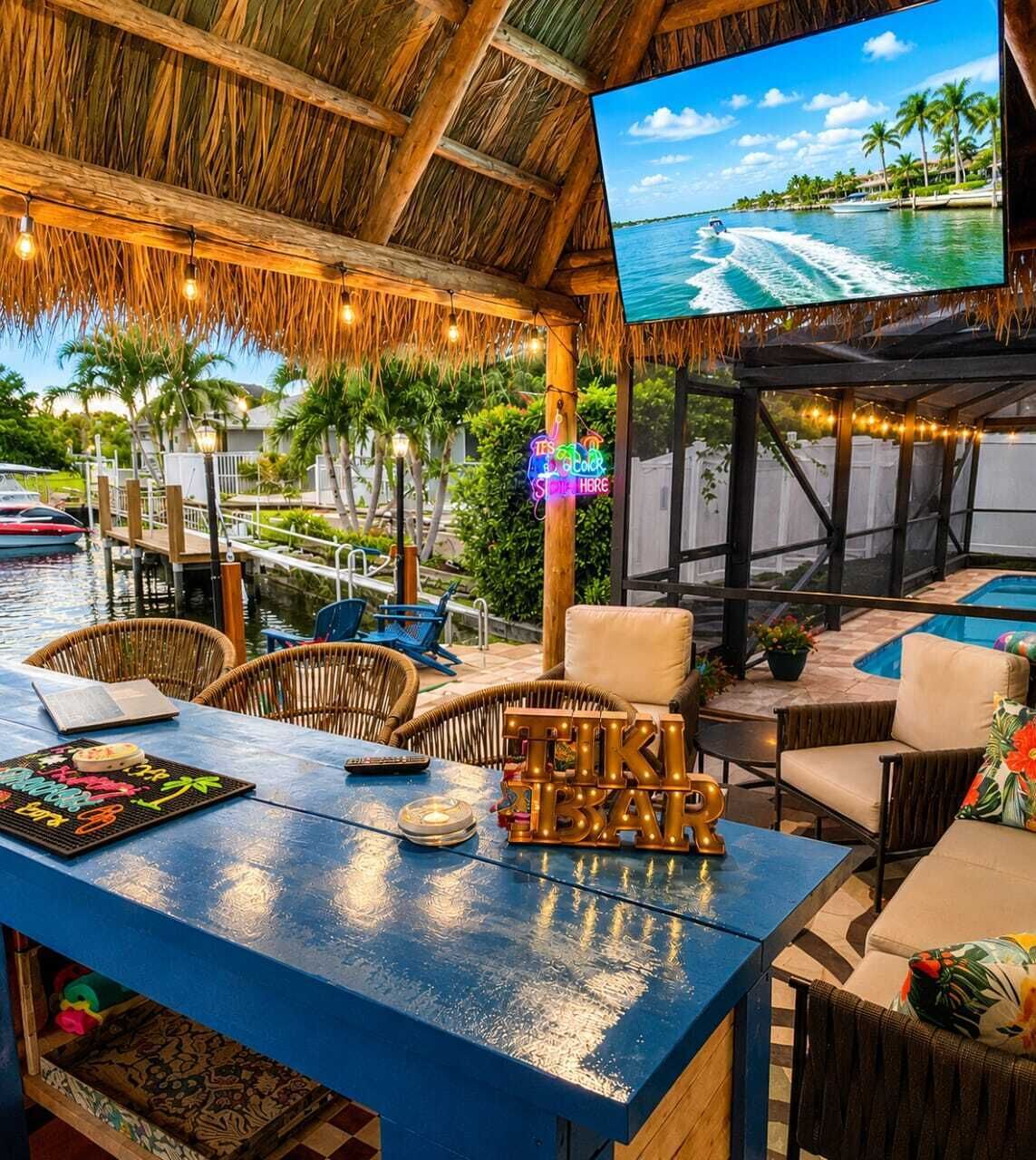 A bar area with a pool, outdoor seating, and a TV screen displaying a tropical scene.