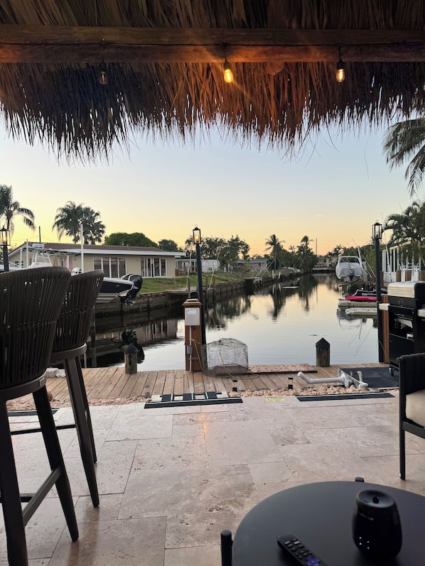 A patio area with chairs, a table, a grill, and a view of a calm water body with boats.
