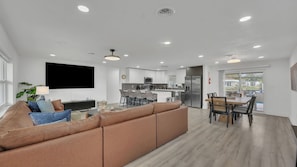 A modern living room with a sofa, a TV, and a kitchen in the background.