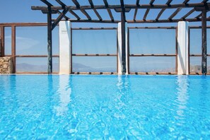 Une piscine d’un bleu éclatant, agrémentée d’une pergola et dotée de grandes fenêtres.