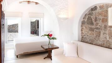 Una camera da letto con un letto, un divano, un tavolino con un vaso di fiori e un muro in pietra.