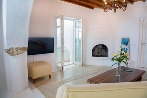 A living room with a television, a fireplace, a bench, and a table with a vase of flowers. - Aegean stones, Ornos, Mykonos (Agios Ioannis Mykonos)