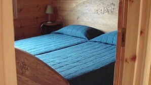 En stuga med träpanel, inredd med två sängar, ett litet bord och en lampa.