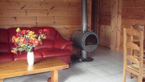 En inredning med trädetaljer, en röd soffa, ett träbord, en vas med blommor och en vedeldad kamin.